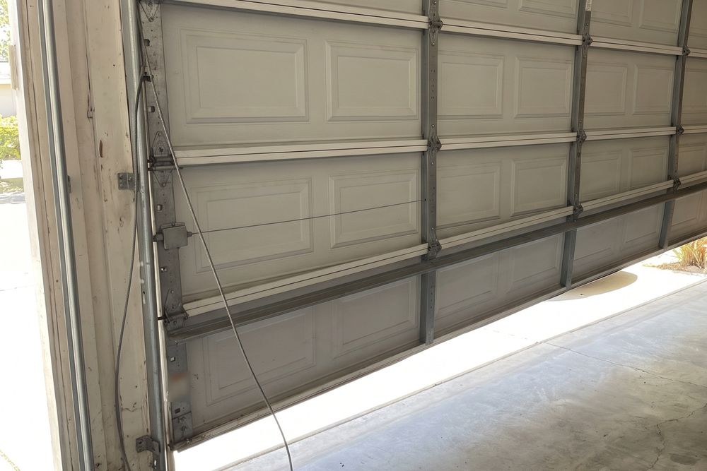 A white sectional garage door hanging crooked with one bottom roller out of its track